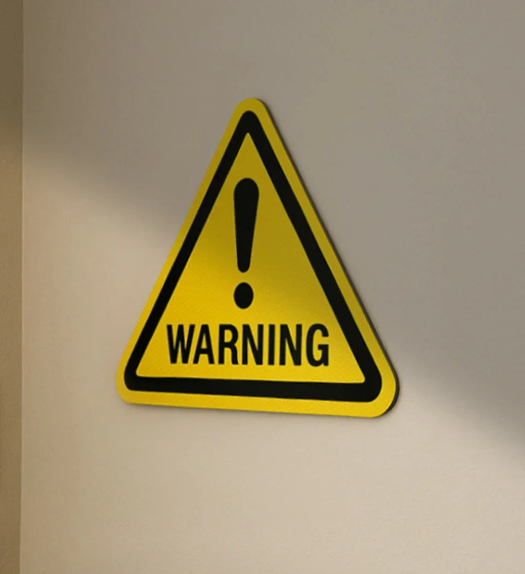 Yellow warning road sign with black border and exclamation mark on a beige wall for modern home decor.