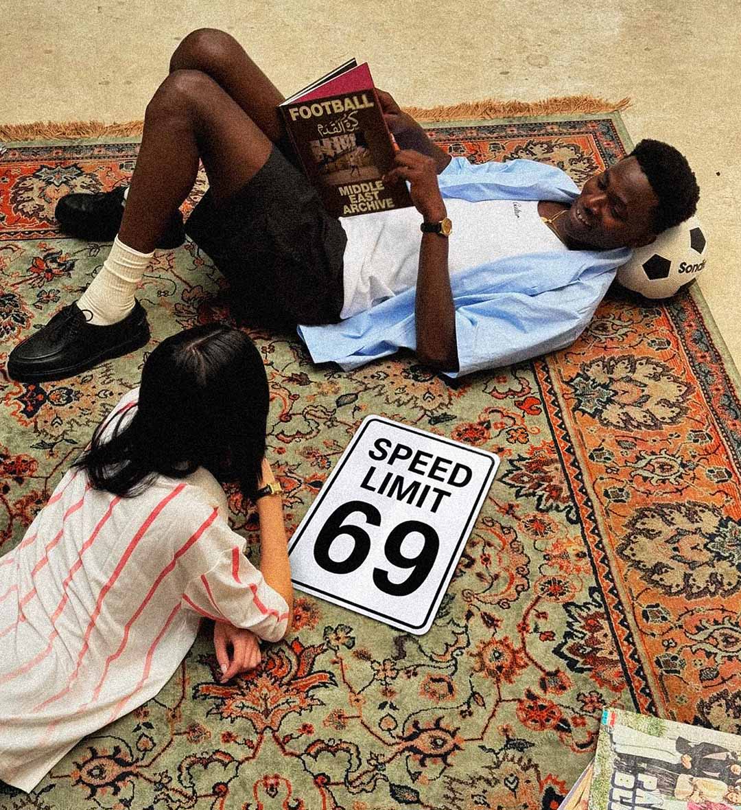Two people lying on a patterned rug with a 'Speed Limit 69' sign between them, pure fun for conversation stater.